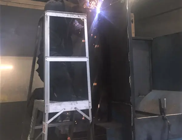 Person, stood on a laddered platform, welding